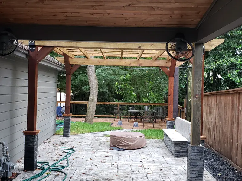 Finished wood pergola over a stone patio with a built-in bench, a covered fire bowl and two wall fans