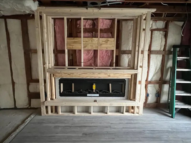 Timber-framed fireplace surround around a long black firebox, insulation still in the studs